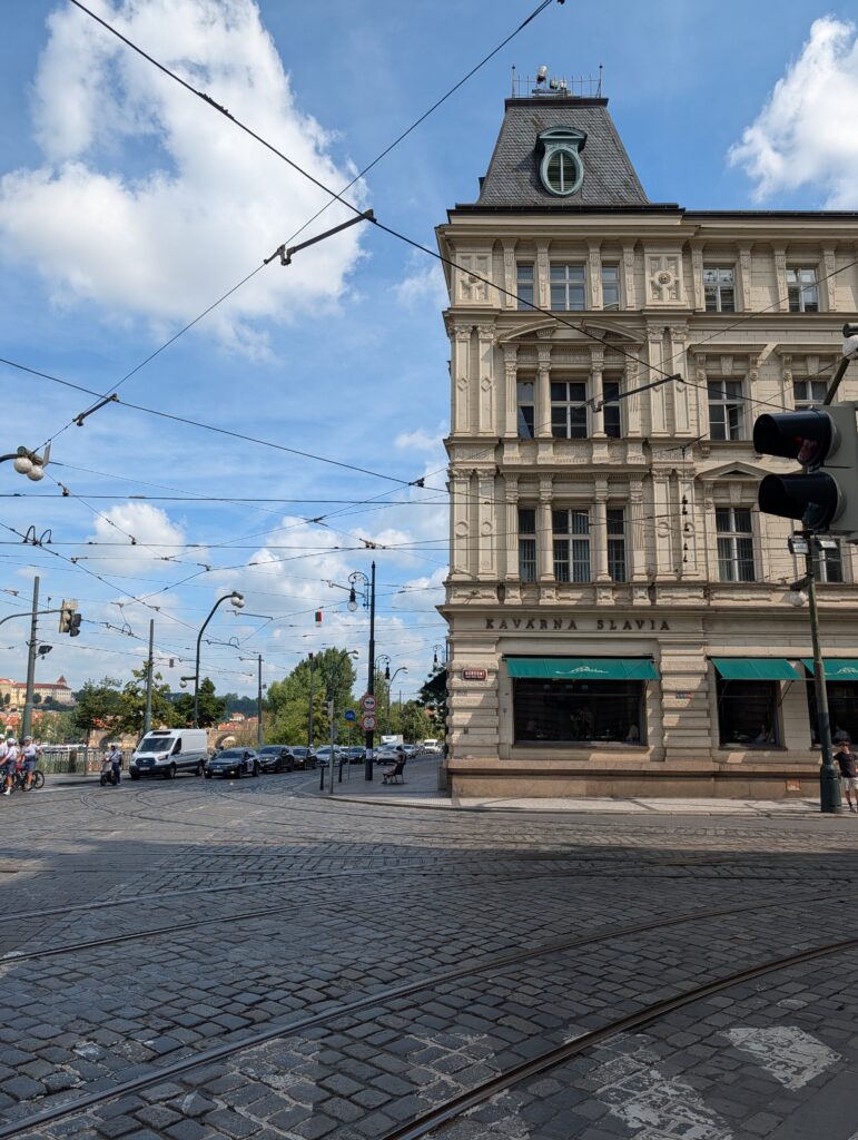 Café Slavia in einem historischen Eckgebäude in Prag mit Straßenbahngleisen und Oberleitungen