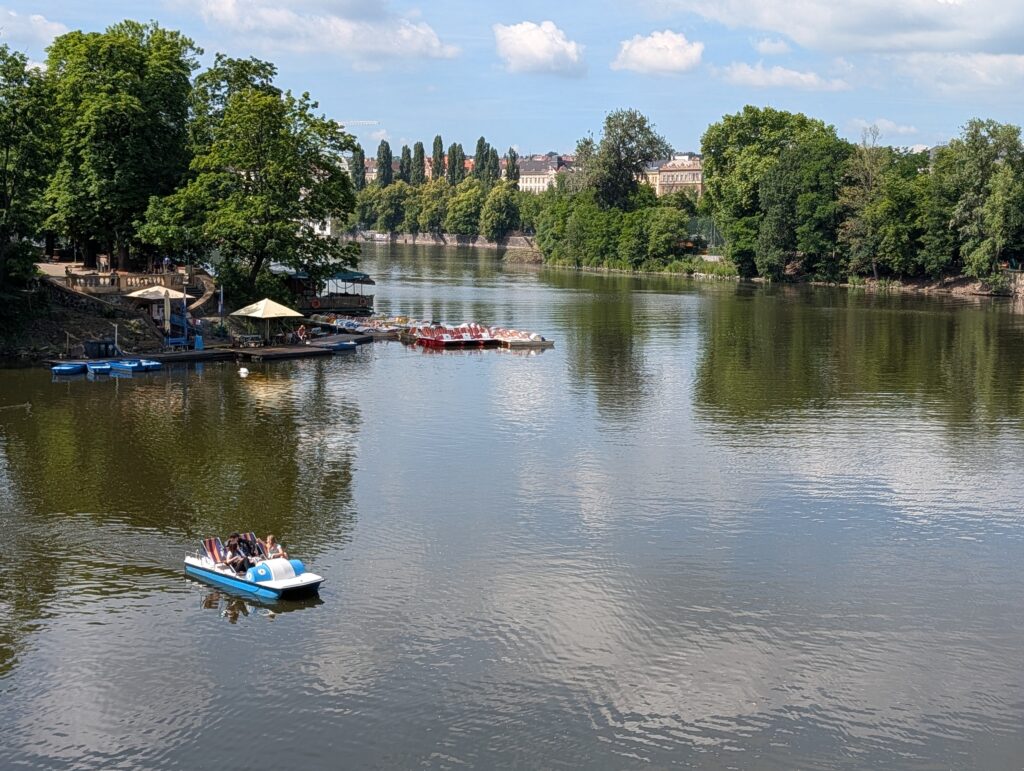 Blau-weißes Tretboot mit mehreren Personen auf der Moldau in Prag