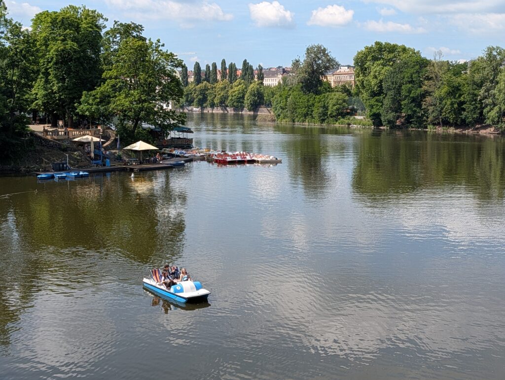 Blau-weißes Tretboot mit mehreren Personen auf der Moldau in Prag
