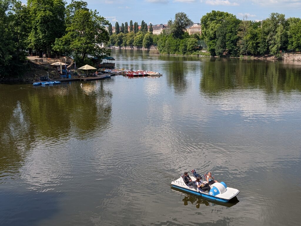 Blau-weißes Tretboot mit mehreren Personen auf der Moldau in Prag