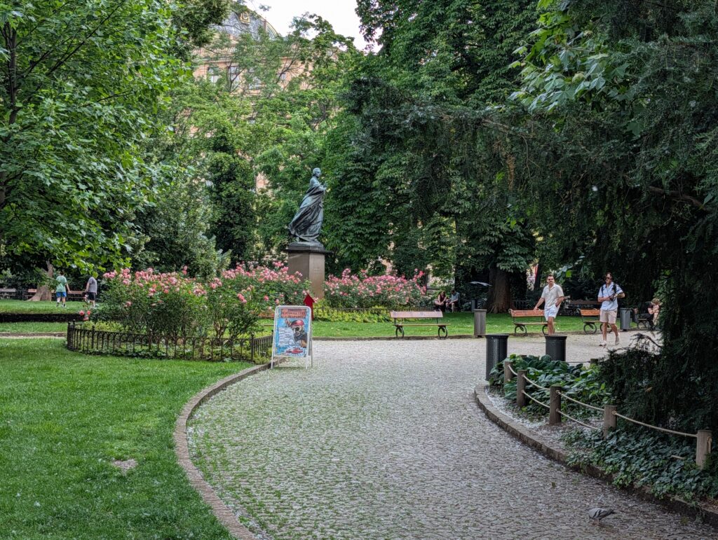 Geschwungener Parkweg mit Rosen, Bänken und Statue auf der Slawischen Insel in Prag