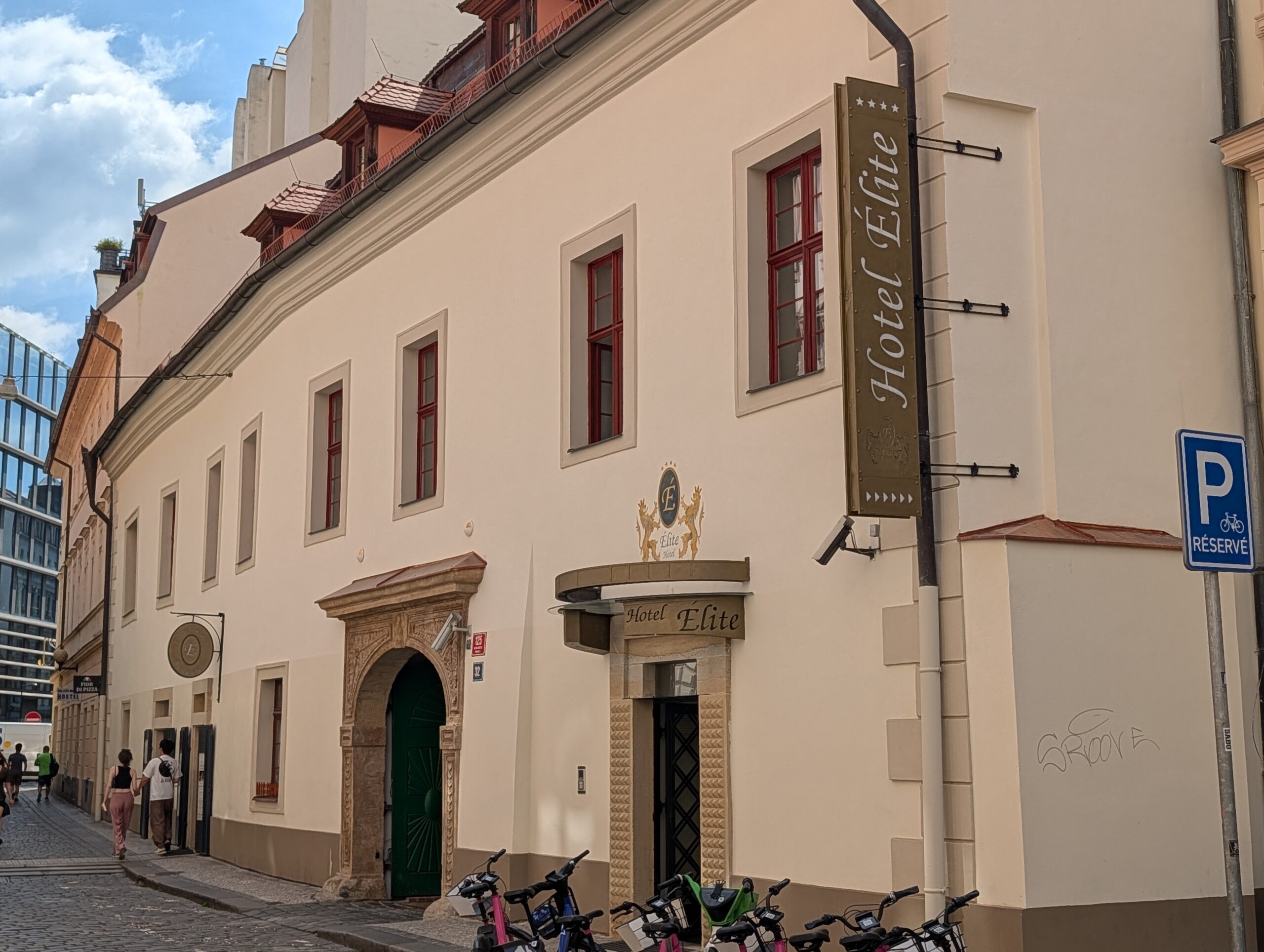 Helle Fassade des Hotel Élite in Prag mit steinernem Eingangsportal und roten Fensterrahmen
