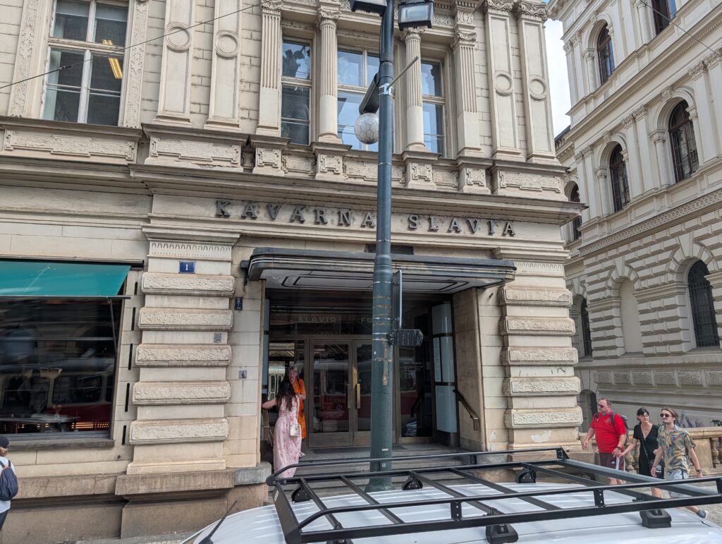 Eingang zum Café Slavia in Prag mit Schriftzug über dem Portal und mehreren Personen