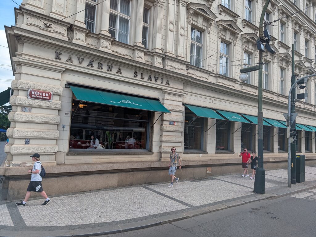 Fassade des Café Slavia in Prag mit grünen Markisen, großen Fenstern und Fußgängern