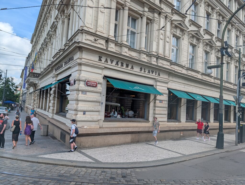 Historisches Eckgebäude des Café Slavia in Prag mit grünen Markisen und Fußgängern