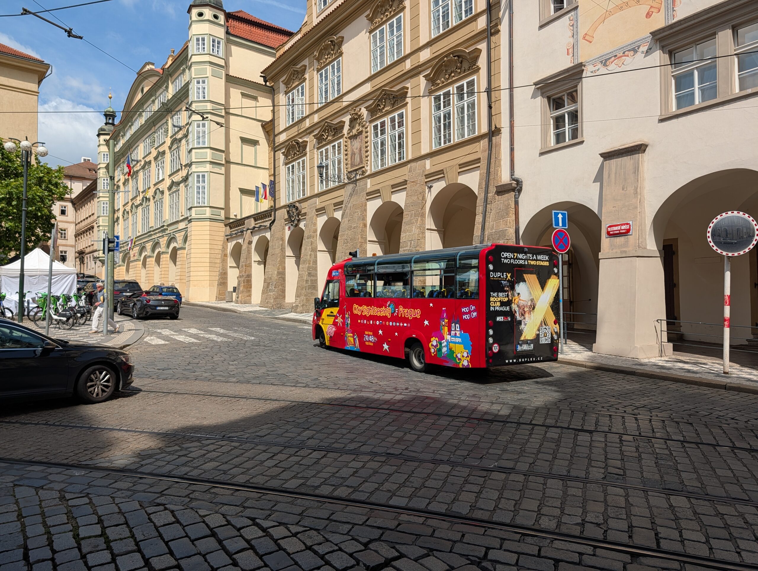Roter City-Sightseeing-Bus auf einer gepflasterten Straße zwischen historischen Gebäuden in Prag
