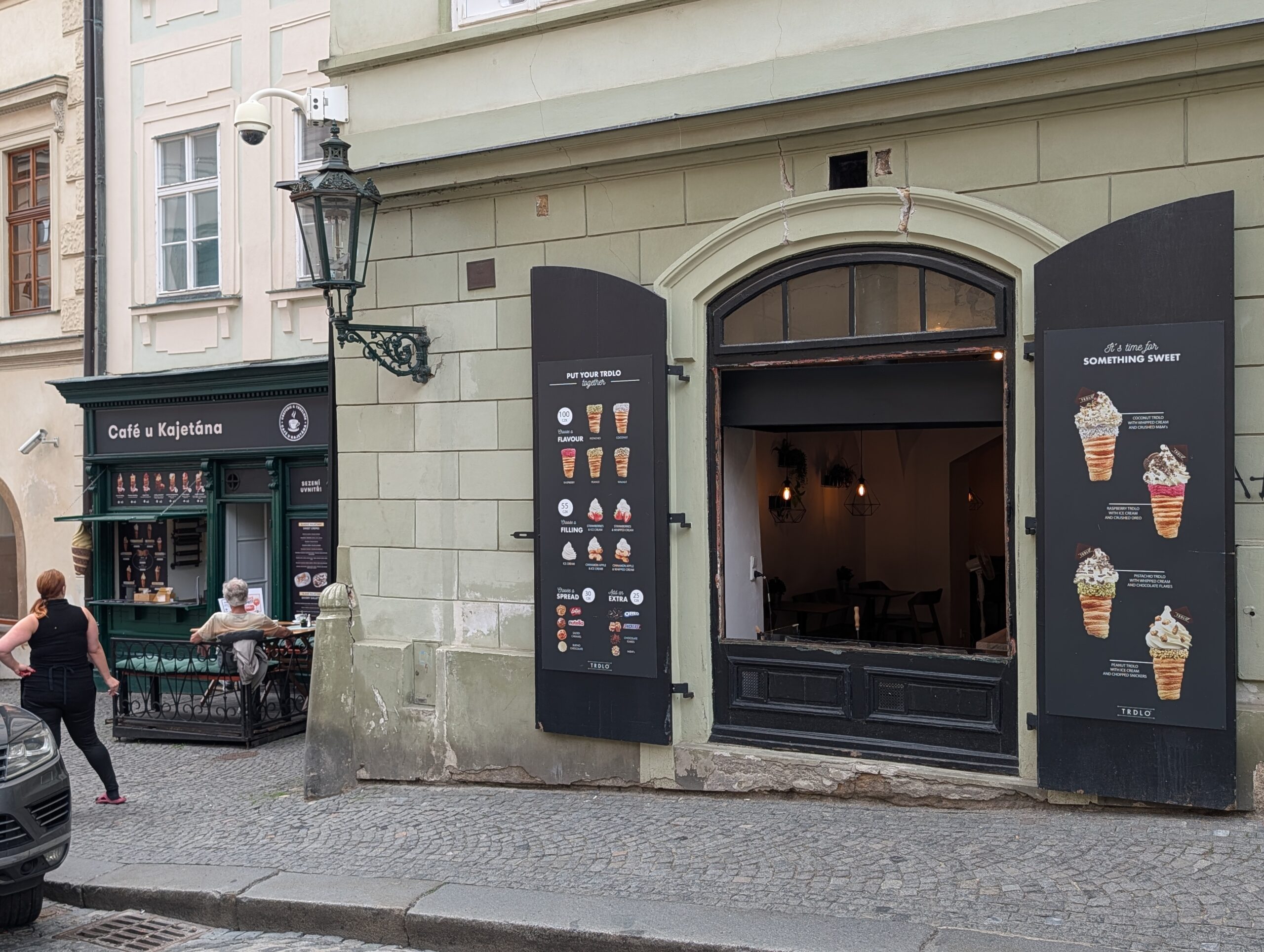 Café U Kajetána mit geöffnetem Verkaufsfenster, Angebotstafeln und Sitzplätzen in Prag