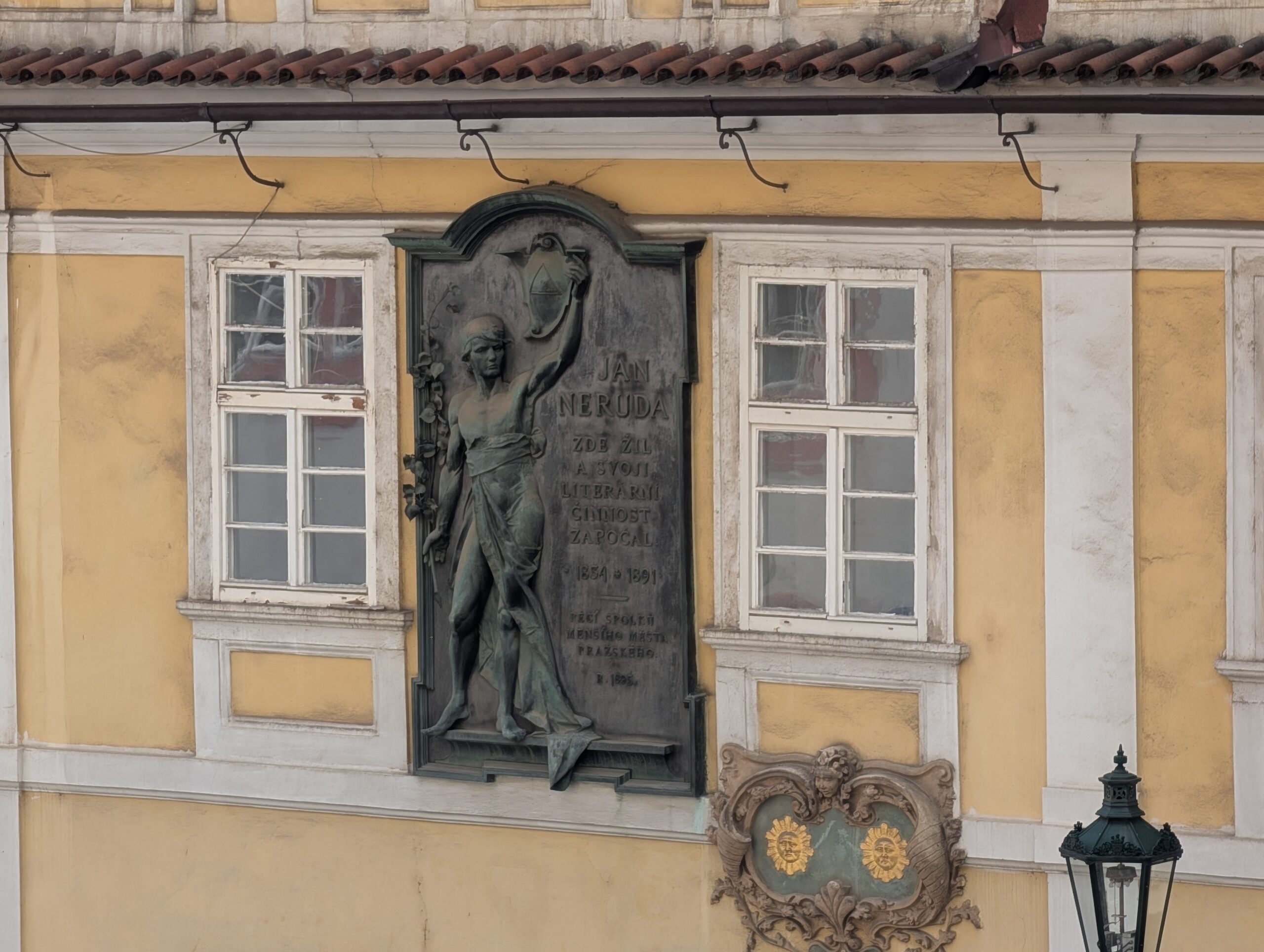 Gedenktafel für Jan Neruda mit Figur und Inschrift an einer gelben Hausfassade in Prag