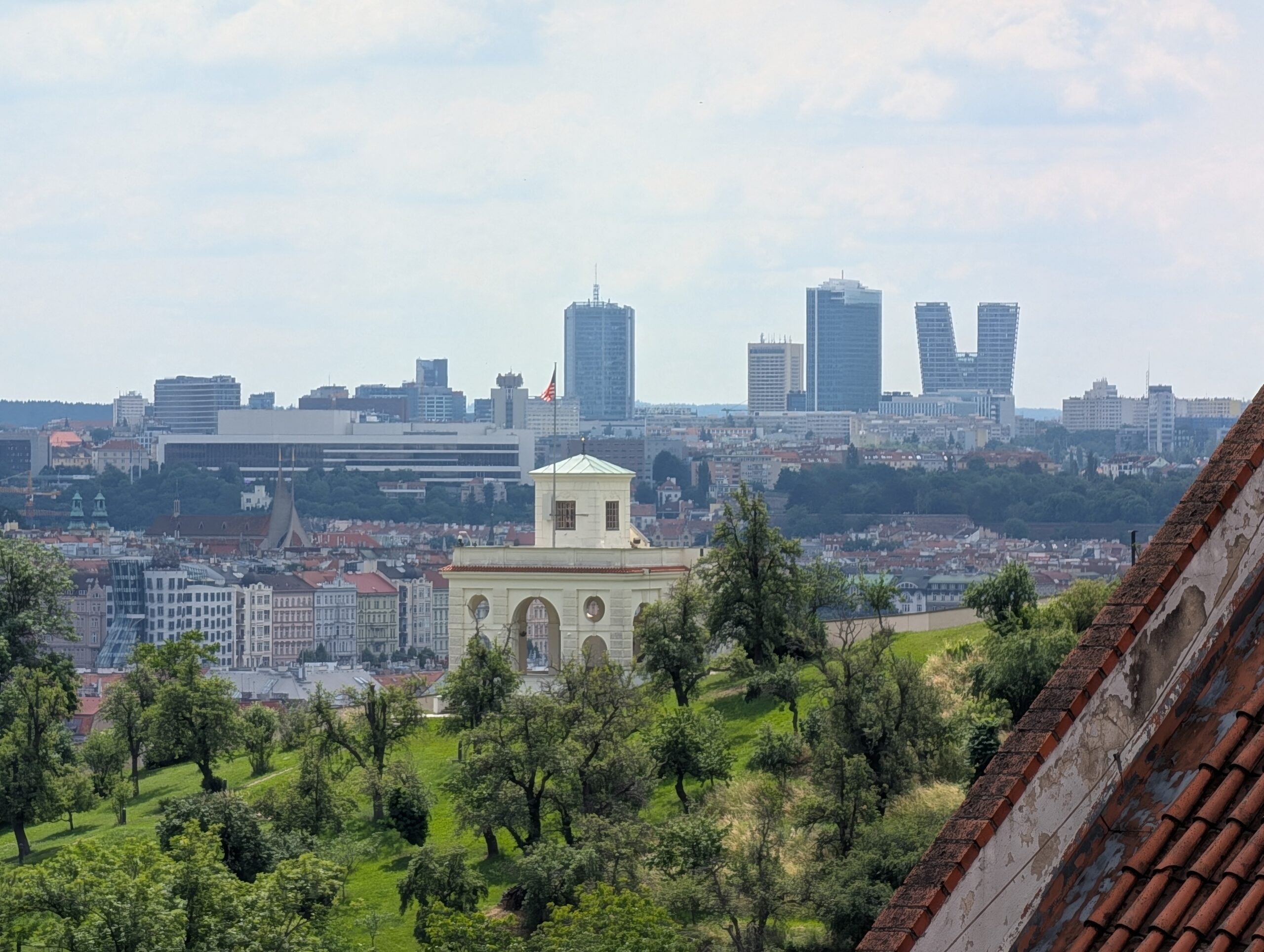 Blick vom Hradschin über grüne Hänge und historische Gebäude zur Skyline von Pankrác