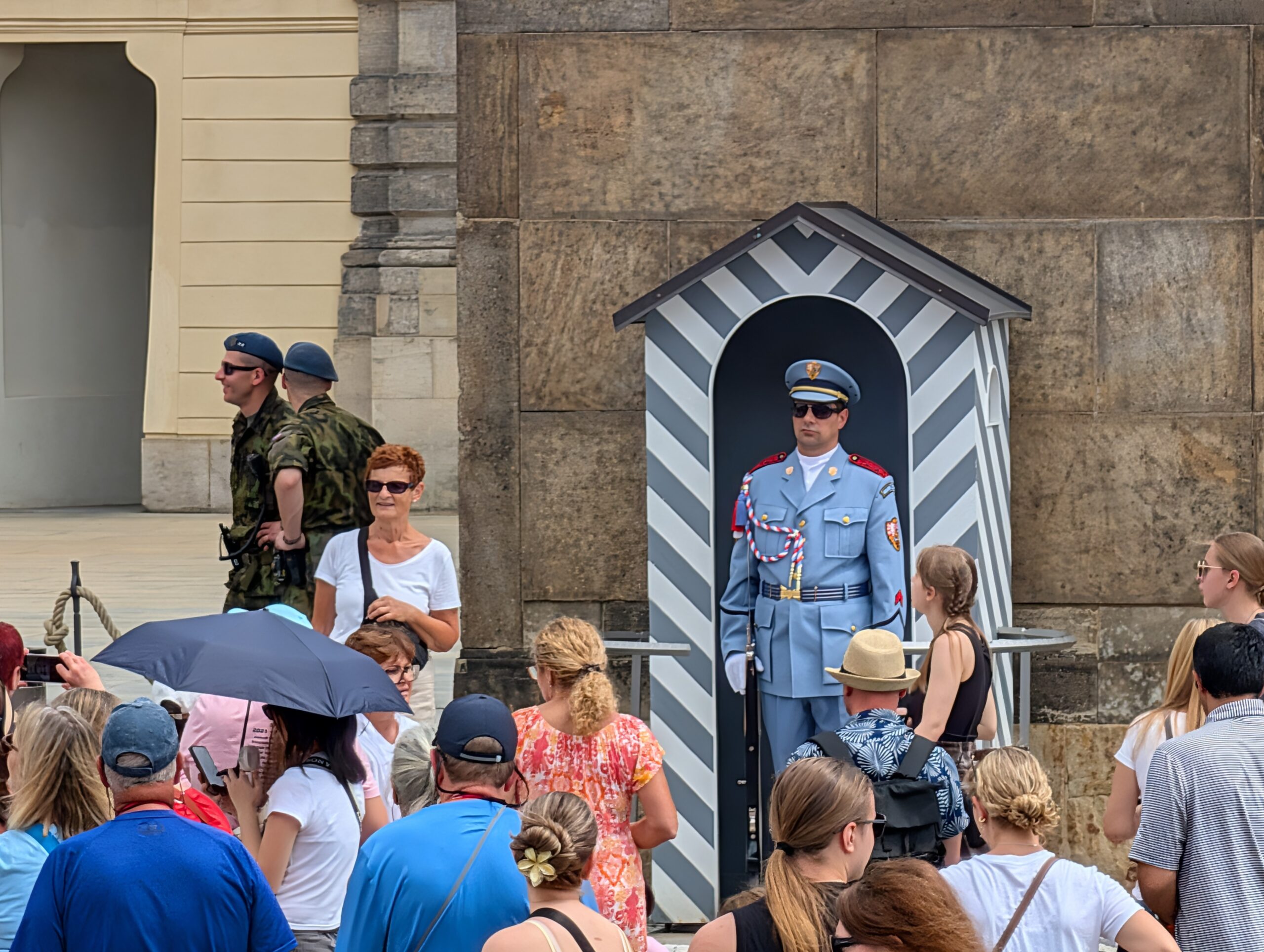Soldat der Burgwache vor einem gestreiften Wachhäuschen mit zahlreichen Besuchern an der Prager Burg