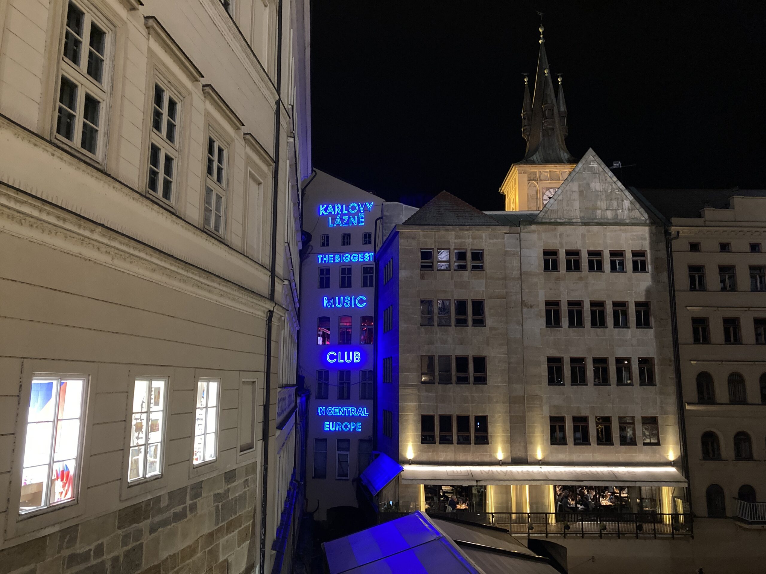 Nächtlich beleuchtetes Gebäude von Karlovy lázně mit blauem Schriftzug nahe der Karlsbrücke in Prag.