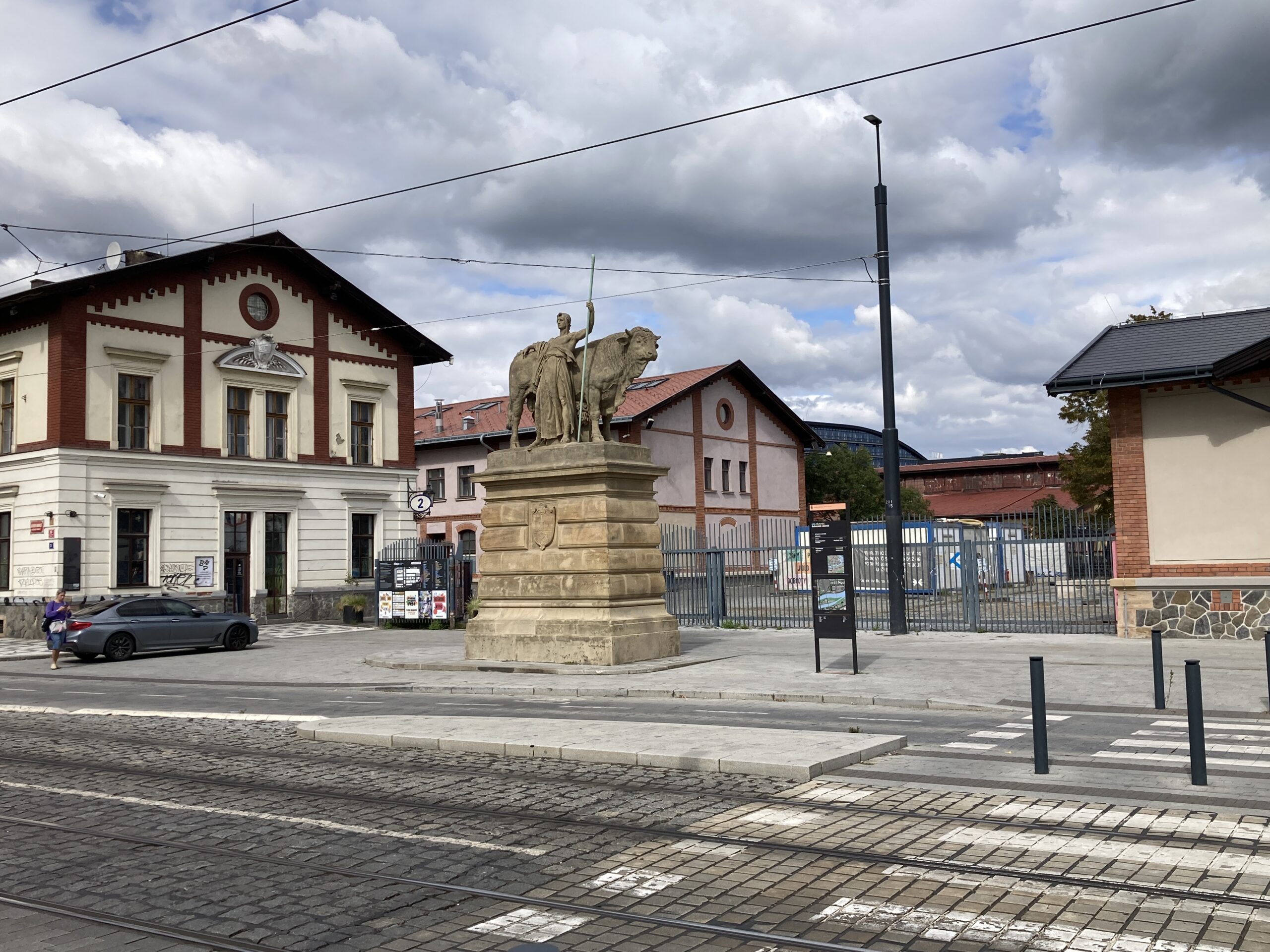 Holešovice-Markt in Prag mit historischen Gebäuden, Tierdenkmal und Straßenbahngleisen im Vordergrund.