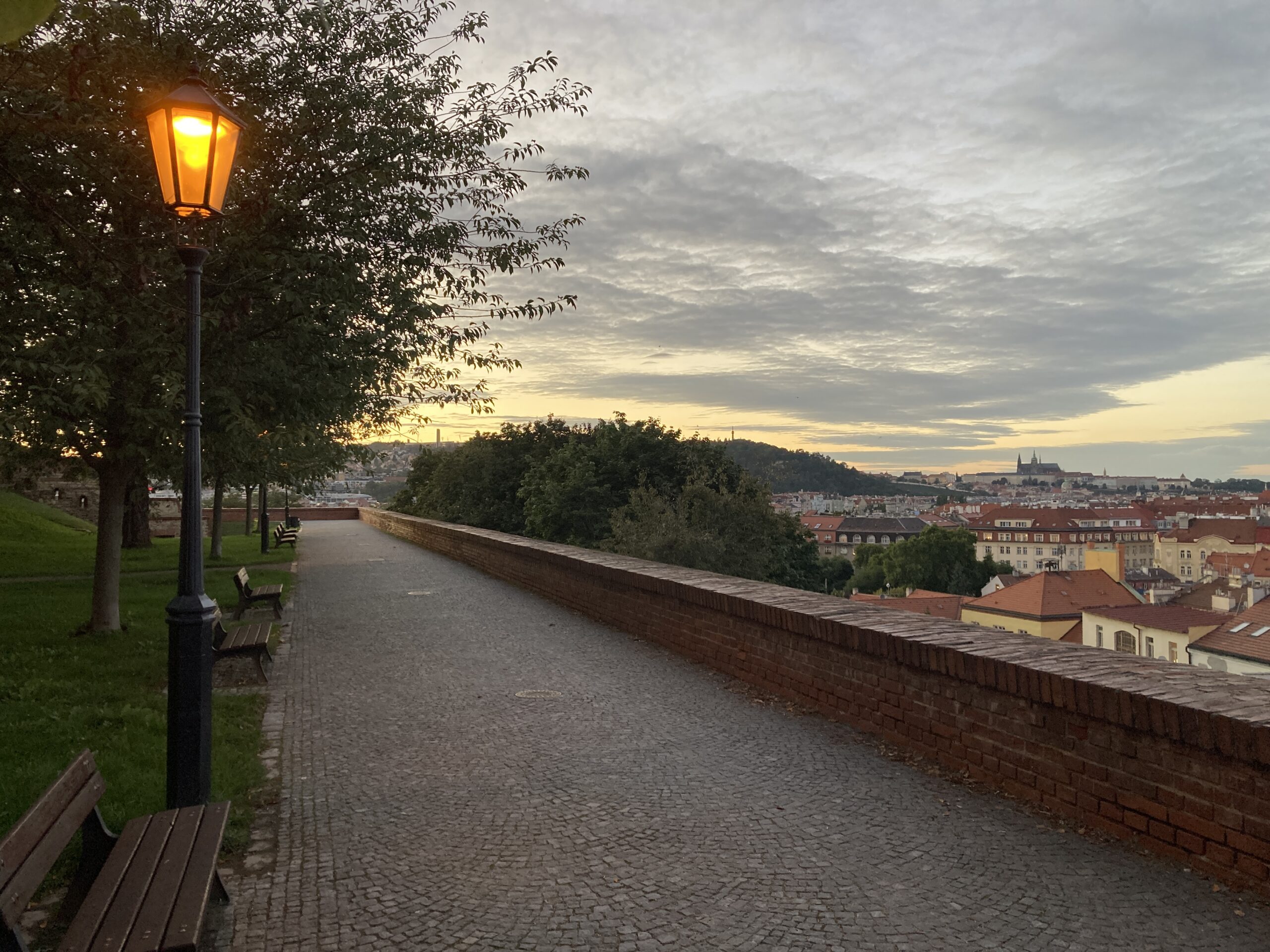 Beleuchteter Weg auf dem Vyšehrad mit Laterne und Blick über Prag zur Prager Burg