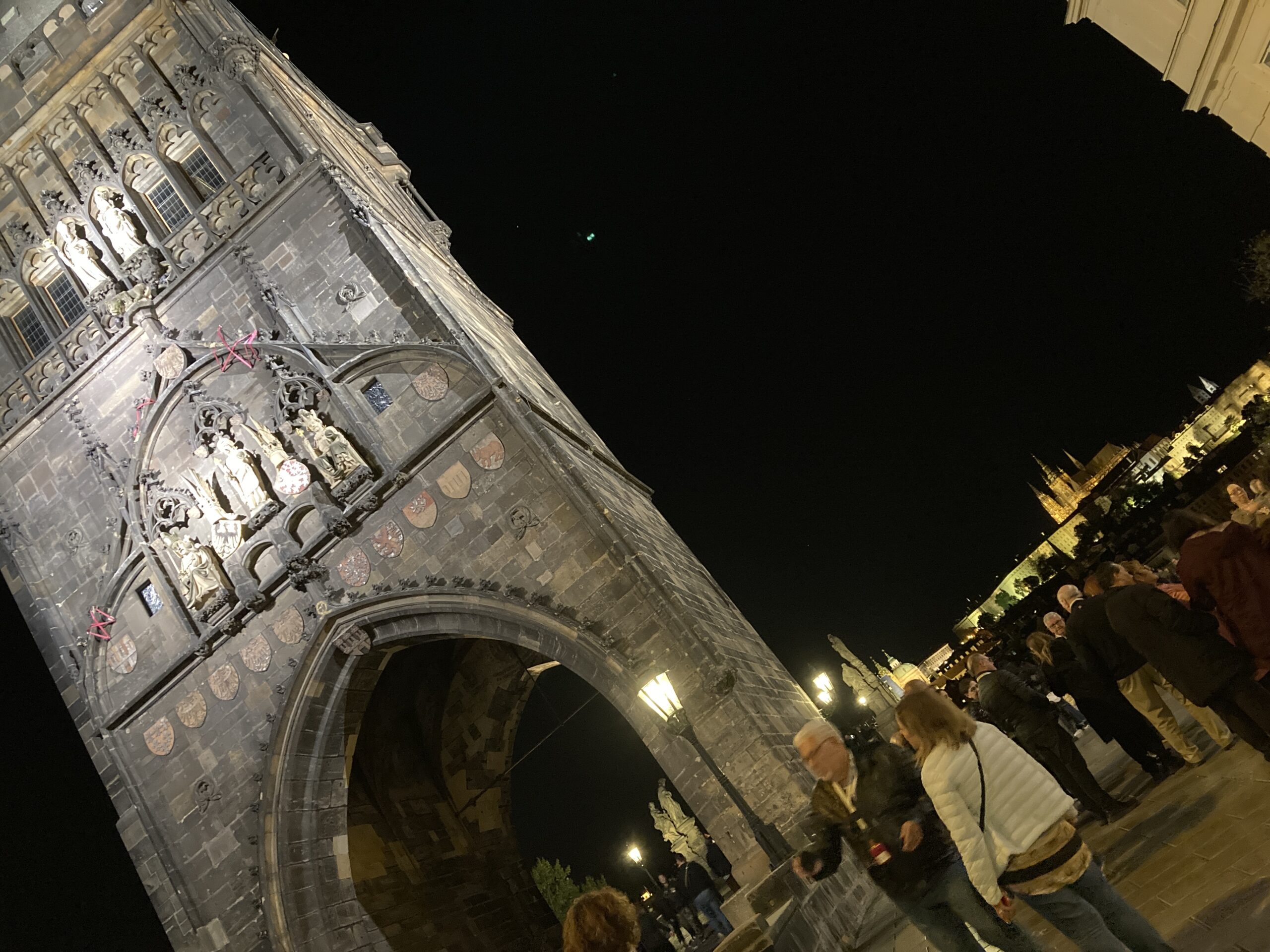 Beleuchteter Altstädter Brückenturm mit Torbogen und Besuchern am Kreuzherrenplatz in Prag