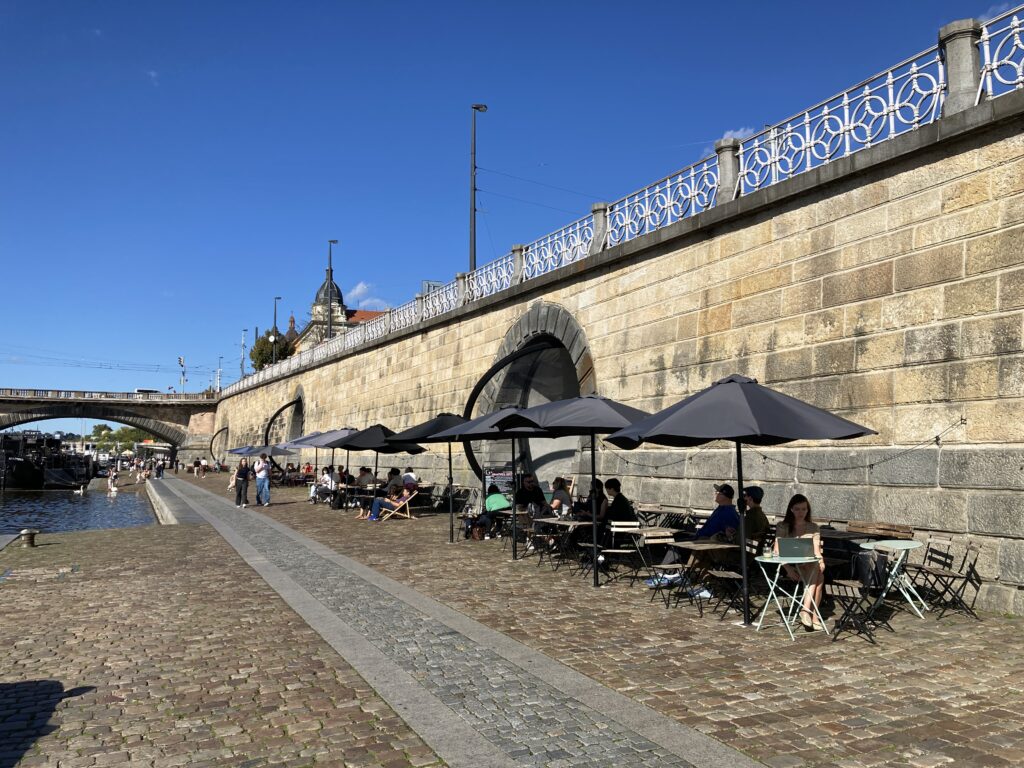 Außengastronomie mit Tischen und Sonnenschirmen an der Náplavka am Moldauufer in Prag